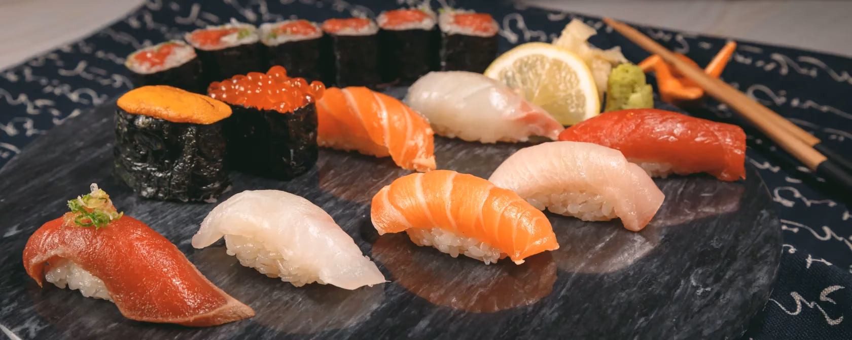 Nigiri of tuna, salmon, yellowtail and white fish, sea urchin and salmon roe, and a tuna roll on a stone plate